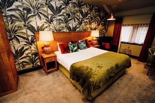 Una habitación de hotel con una cama grande, dos mesitas de noche con lámparas, una pequeña mesa con lámpara, una silla y una ventana con cortinas.