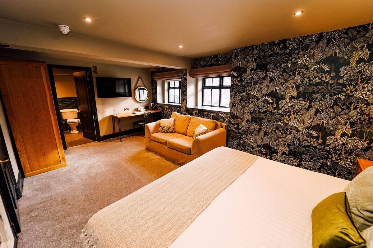 A hotel room with a bed, a sofa, a desk, a TV, and a bathroom.
