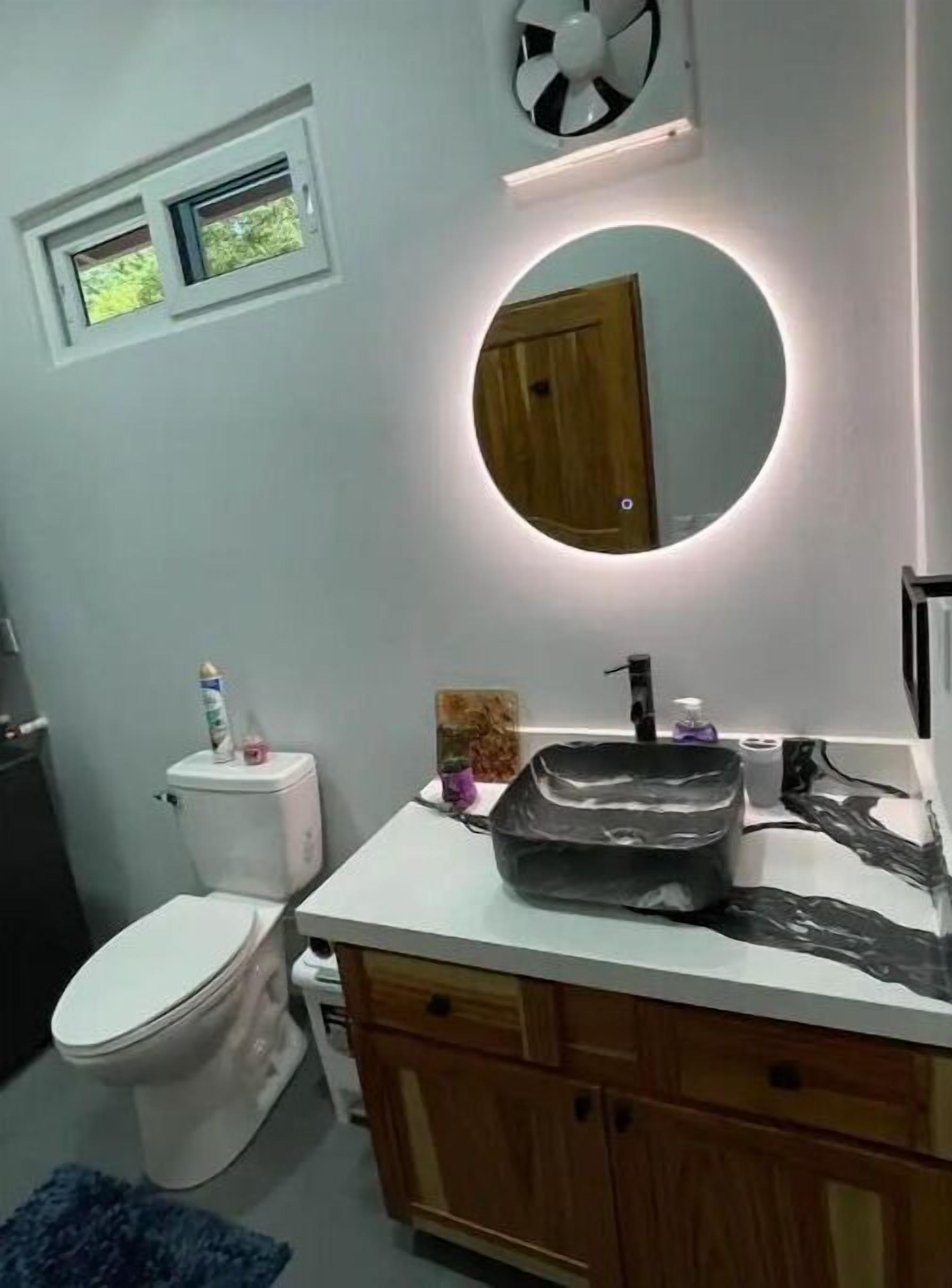 Une salle de bain équipée de toilettes, d’un lavabo avec un miroir et d’un ventilateur au plafond.