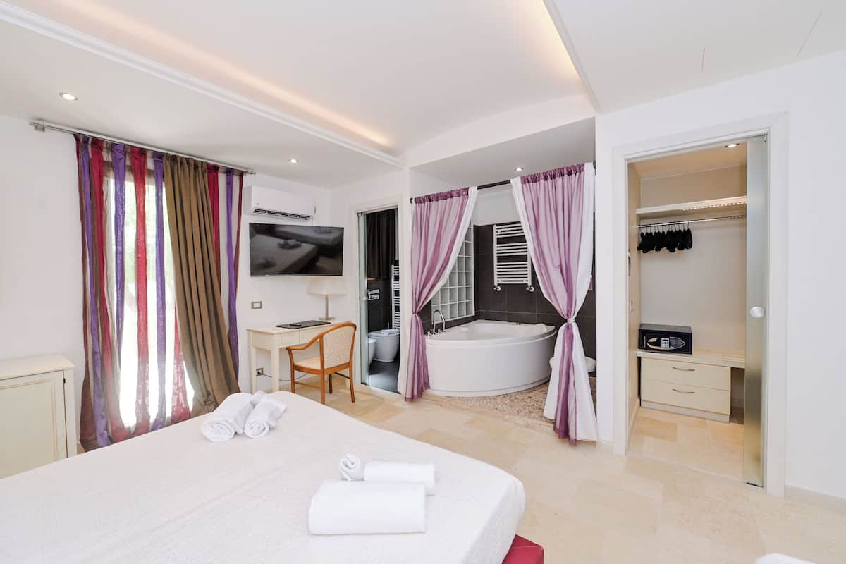 A modern hotel room with a large bed, a desk, a chair, a bathroom with a bathtub, and a walk-in closet.