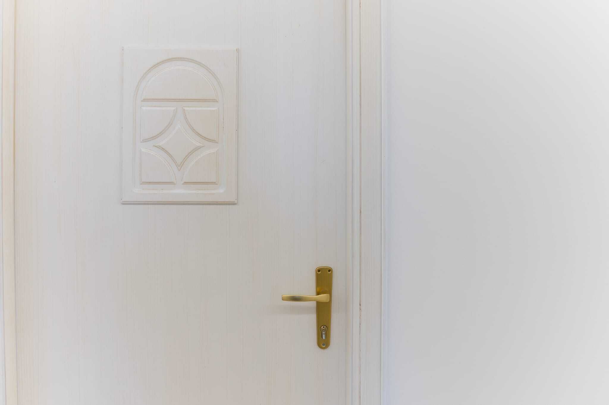 Une porte blanche avec une poignée de porte en laiton et un panneau décoratif.