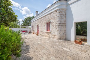 Un edificio de piedra con fachada blanca, un patio empedrado y plantas en macetas.