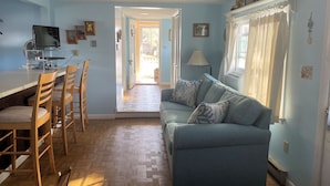 A room with a blue sofa, wooden chairs, a TV, and a dining table.