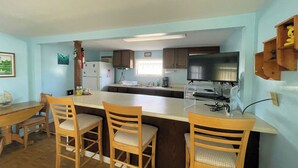 A kitchen with a bar area, wooden chairs, a refrigerator, a microwave, and a television.