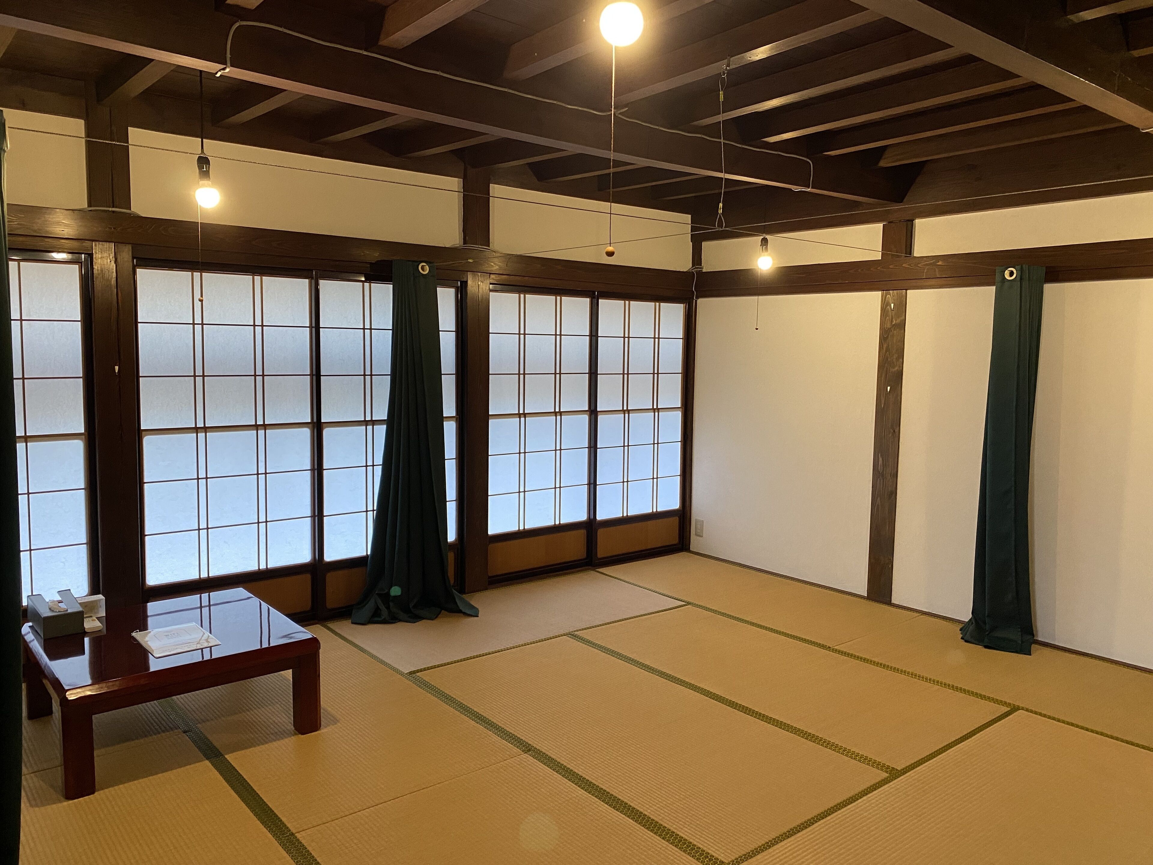 Una habitación tradicional con esteras de tatami, puertas correderas, una mesa de madera y lámparas colgantes.