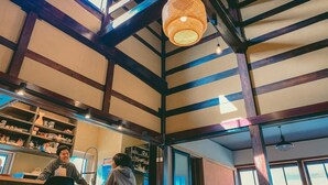 A room with exposed wooden beams, a large woven light fixture, and a person at a counter.