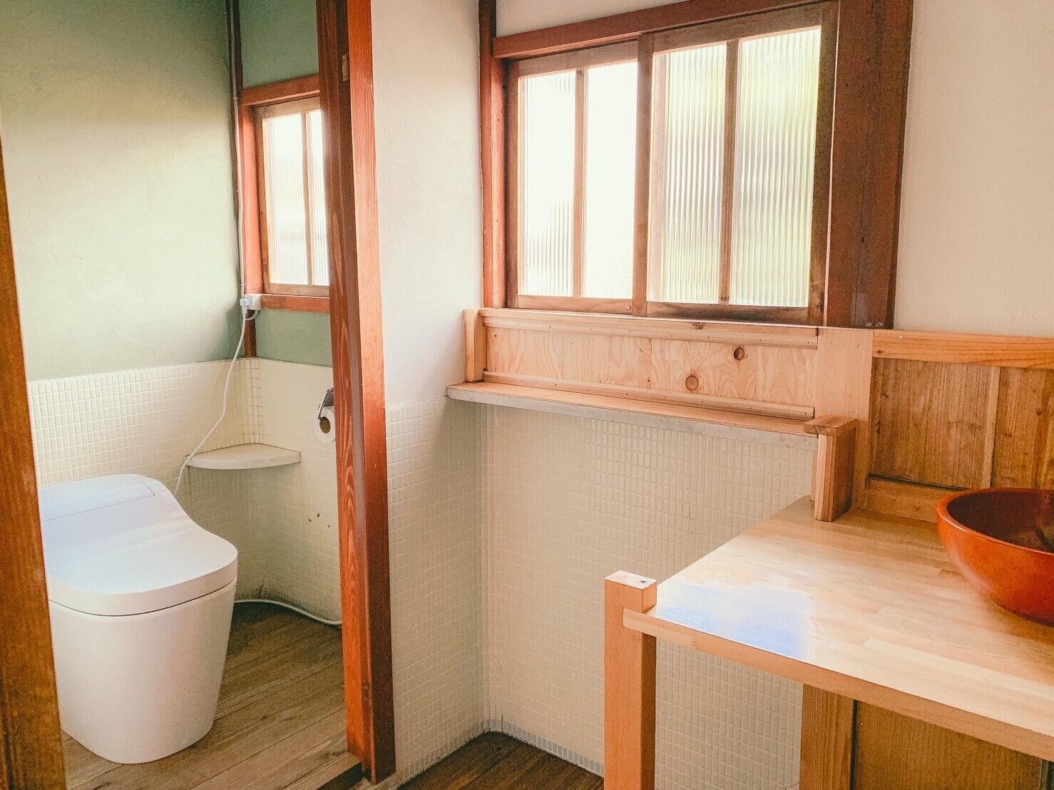 Une petite salle de bain avec des toilettes, une étagère en bois et une fenêtre.