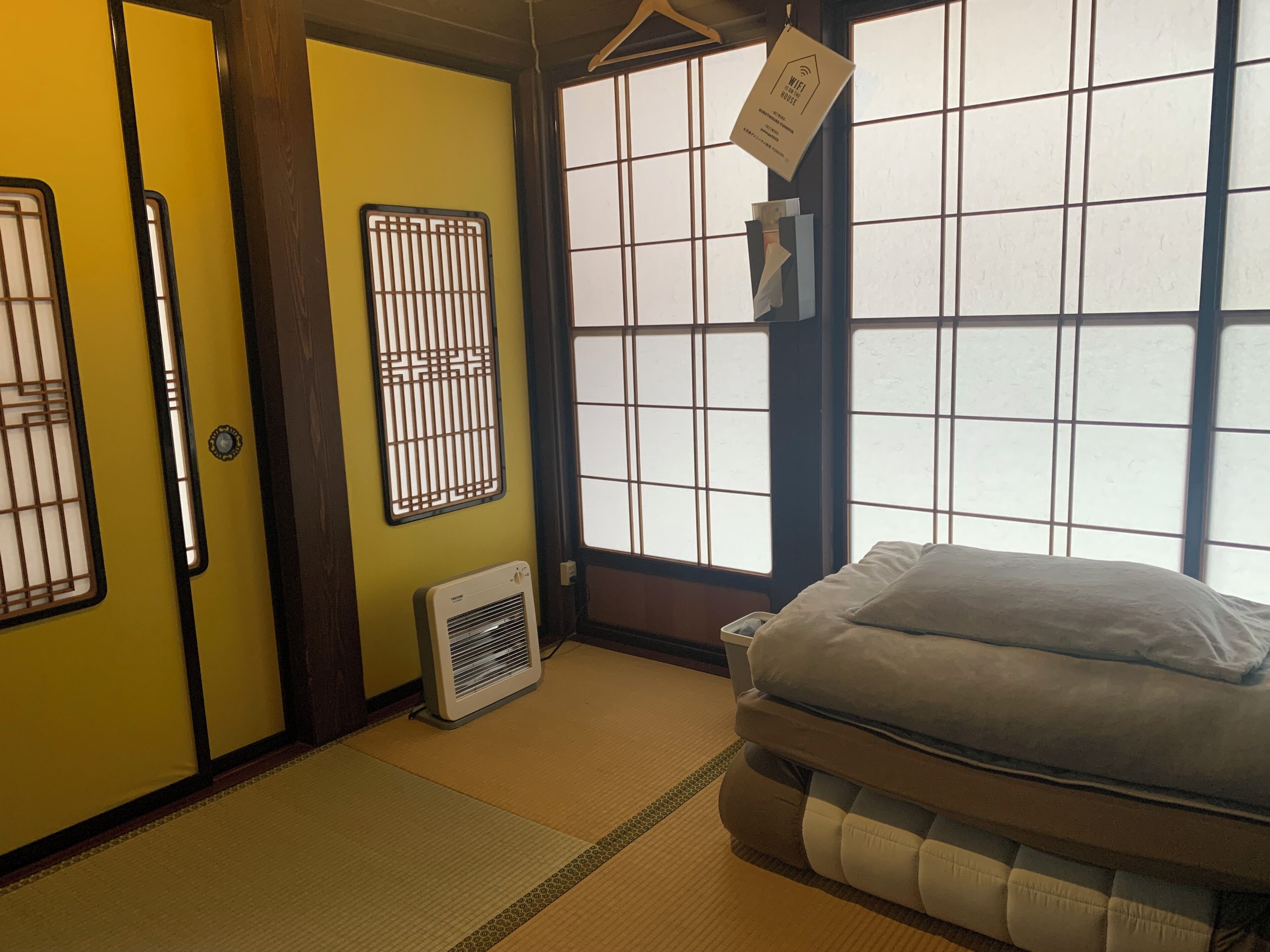 Um quarto tradicional japonês com piso de tatame, futon, porta deslizante, janela com padrão de grade e ar-condicionado fixado na parede.