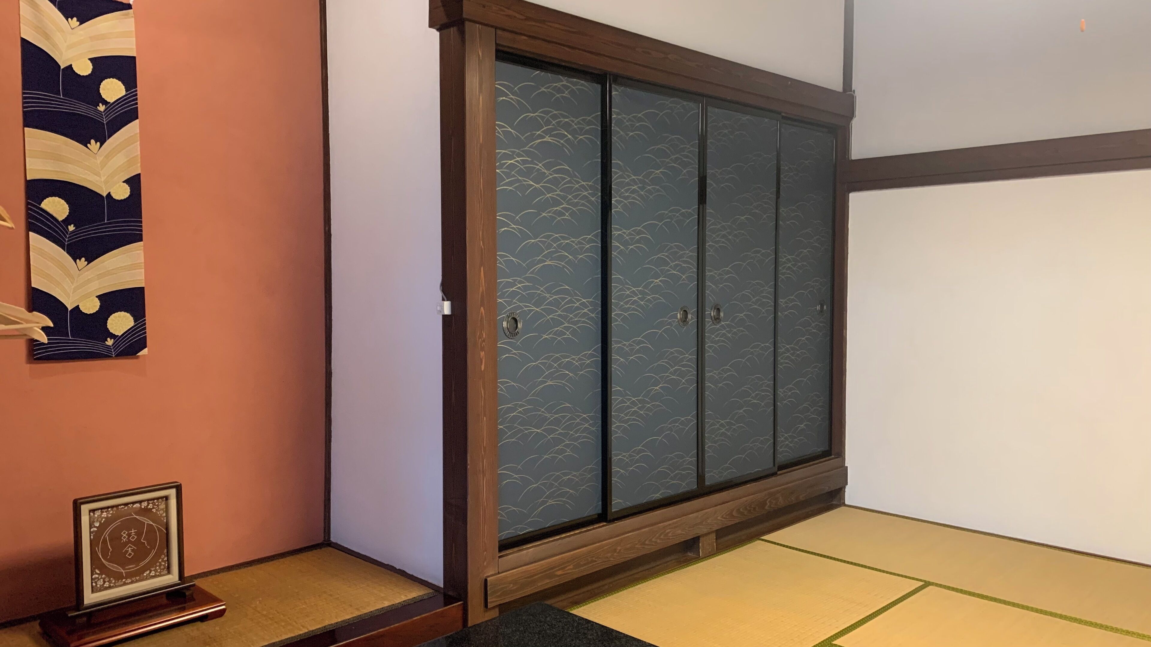 Um quarto japonês tradicional com tatames, uma porta deslizante com padrão de ondas e um painel de caligrafia emoldurado no chão.