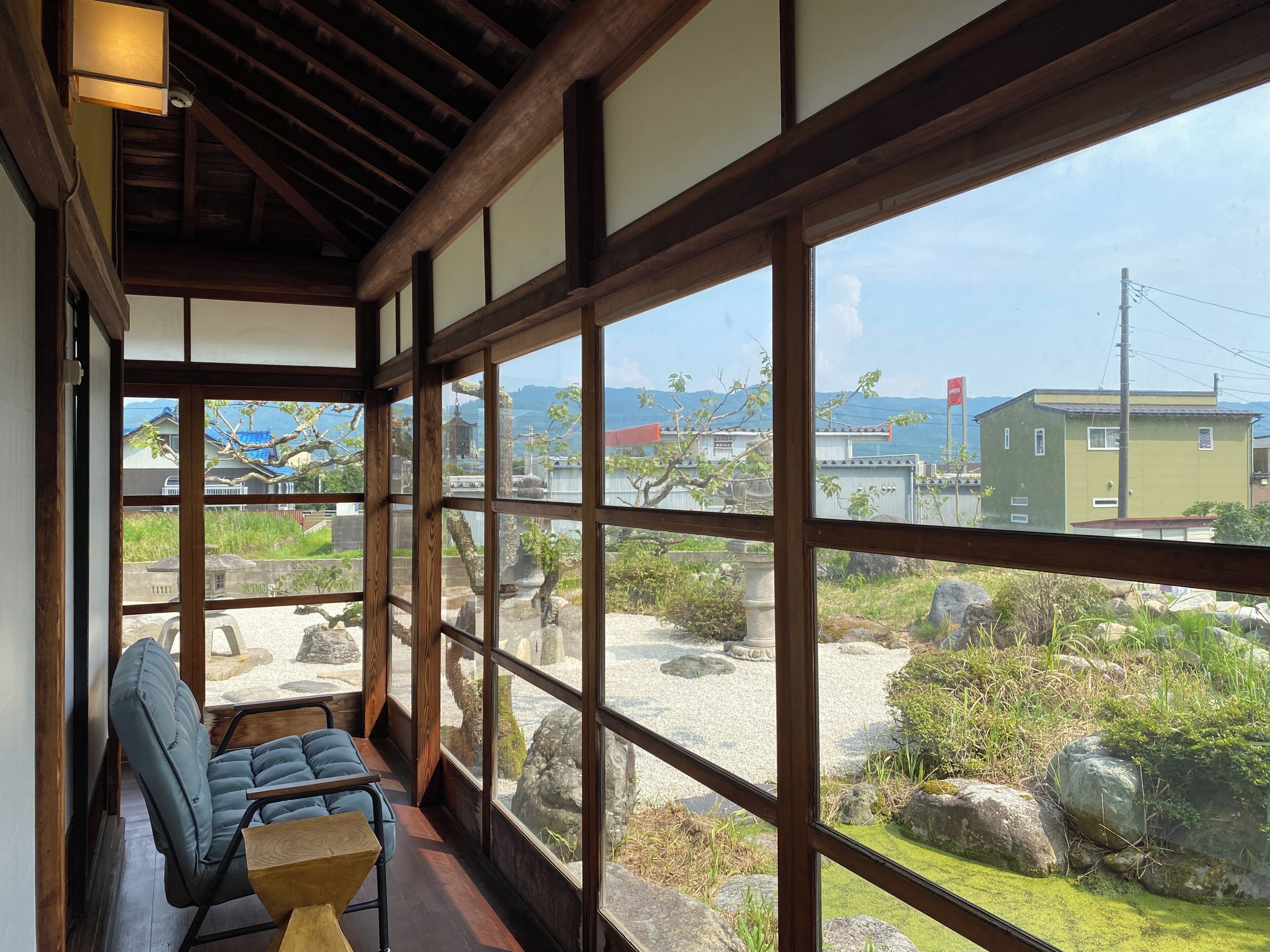 Um quarto japonês tradicional com tatames, teto de madeira e grandes janelas com vista para um jardim e edifícios.