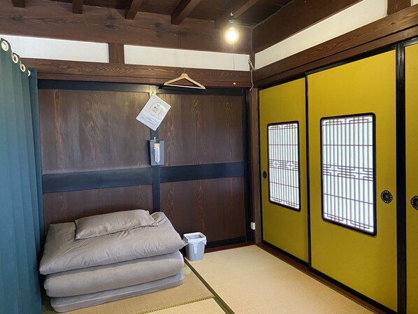 Una habitación japonesa tradicional con suelo de tatami, un futón, puertas correderas y una lámpara colgante.