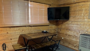 A wooden-paneled room with a table and benches, a flat-screen TV mounted on the wall, and a heater. - One Bedroom Cabin with Ample Parking and Space from Neighboring Cabins (Almont)