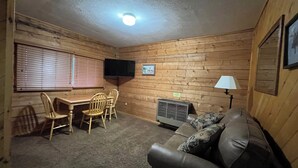 A cozy room with wooden walls, a leather couch, a table with chairs, a TV, and a heater. - One Bedroom Cabin with Ample Parking and Space from Neighboring Cabins (Almont)