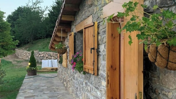 Un bâtiment en pierre avec des volets en bois et un chemin de pierre menant à l’entrée.