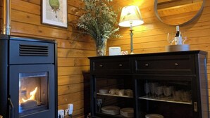 Une pièce aux murs lambrissés, avec une cheminée, un miroir, une lampe et un buffet contenant de la vaisselle.