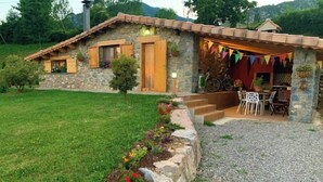 Une maison en pierre avec un toit en tuiles, un petit porche à l’avant doté de sièges extérieurs et une allée gravillonnée.