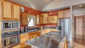 Una cocina con armarios de madera, electrodomésticos de acero inoxidable, encimeras de granito y un ventanal con cortinas.