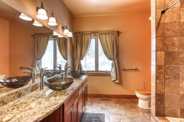 A bathroom with a granite countertop, two vessel sinks, a toilet, and a shower area. - Westwinds Lodge – Stunning Views, Hot Tub & Cozy Retreat (Lead)