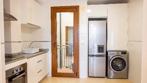 Cocina compacta con armarios blancos, un refrigerador de acero inoxidable, una lavadora y una puerta de madera.