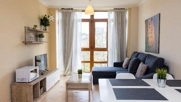 Una sala de estar moderna con un sofá, una mesa de comedor, un televisor y un ventanal con cortinas.