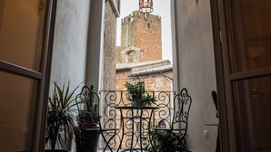 Un arco de entrada da a un patio con suelo de baldosas, plantas en macetas y una mesa y sillas de hierro forjado.
