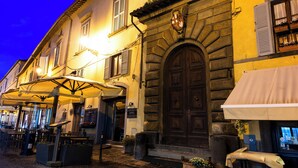 Un café al aire libre con mesas y sombrillas, un edificio de piedra con una puerta de madera grande y un cartel sobre la puerta.