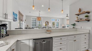 Une cuisine spacieuse avec des meubles blancs, un grand îlot central et des luminaires suspendus.