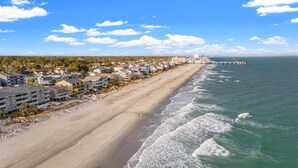 Une ville côtière dotée de propriétés en bord de mer, d’une jetée s’avançant dans l’océan et d’un ciel dégagé.