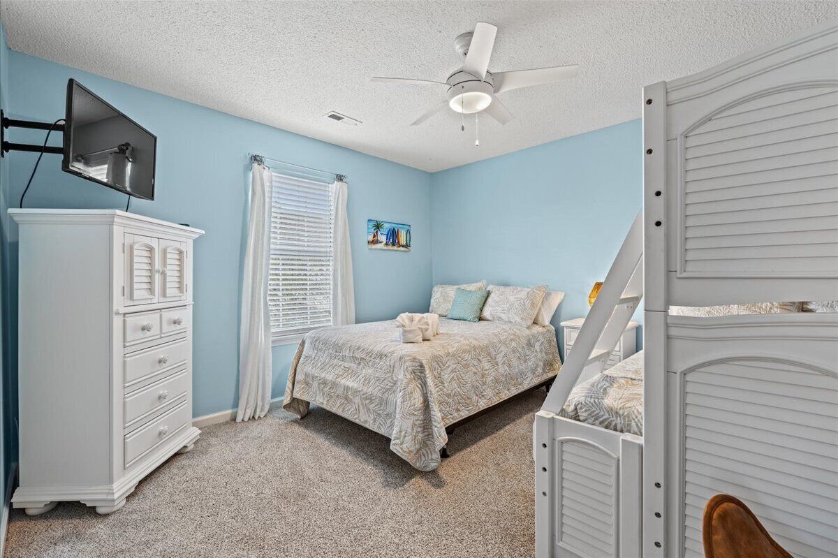 A bedroom with a bed, a dresser, a ceiling fan, and a window with blinds.