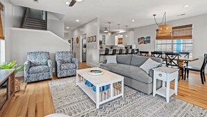 Un salon moderne avec un canapé gris, des fauteuils à motifs, une table basse et un coin repas comprenant une table et des chaises.