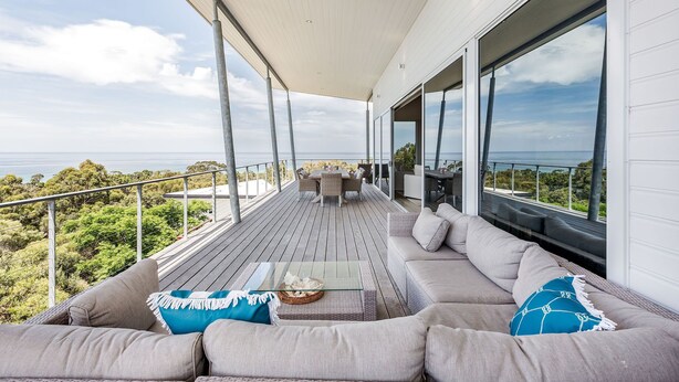 Une terrasse extérieure moderne, dotée d’un canapé, d’une table et d’un coin repas offrant une vue imprenable sur un paysage magnifique.