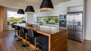 Une cuisine moderne dotée d’un îlot central, d’appareils électroménagers en acier inoxydable et de luminaires suspendus noirs.