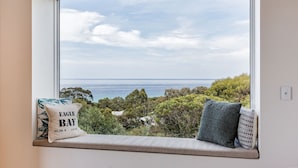 Un siège de fenêtre donnant sur l’océan et les arbres, un coussin portant l’inscription « Eagle Bay », et une petite table.