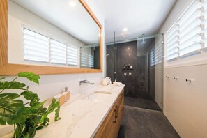A modern bathroom with a large mirror, a sink, and a shower area. - Airlie On Airlie Premier (Airlie Beach)