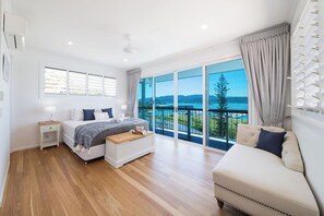 A modern bedroom with a large window, a bed, a bedside table, and a sofa. - Airlie On Airlie Premier (Airlie Beach)
