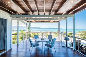 A covered outdoor area with a table and chairs, overlooking a scenic view of a body of water and mountains. - Airlie On Airlie Premier (Airlie Beach)