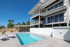 Ein zweistöckiges Gebäude mit Swimmingpool, Sitzgelegenheiten im Freien und einem Holzzaun.