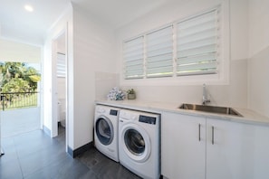 Ein moderner Waschraum mit zwei Waschmaschinen mit Frontlader, einem Waschbecken und einem Fenster mit Jalousien.