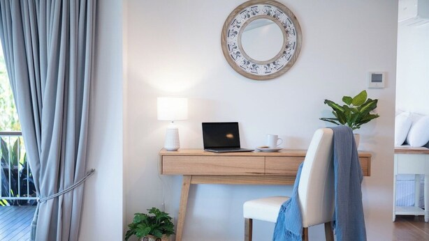 Una stanza con una scrivania, una sedia, un portatile, una lampada, una pianta in vaso e uno specchio decorativo.