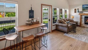 A cozy living room with a fireplace, a wooden dining table with bar stools, and a comfortable sofa. - Dover Bay 'Barefoot Bungalow' | Marina + Trails (Dover)