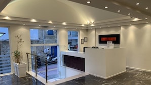Un espace d’accueil moderne avec un sol en marbre, un comptoir d’accueil et une grande fenêtre donnant sur une cour intérieure.