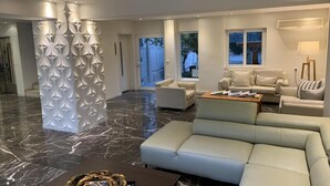 Un salon moderne avec un sol en marbre, un canapé d’angle blanc, un fauteuil beige et une table basse.