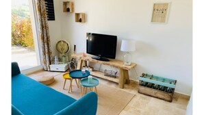 A living room with a blue sofa, two small round tables, a television, and a wooden coffee table. - Gîte le grand chacel (Sourcieux-les-Mines)