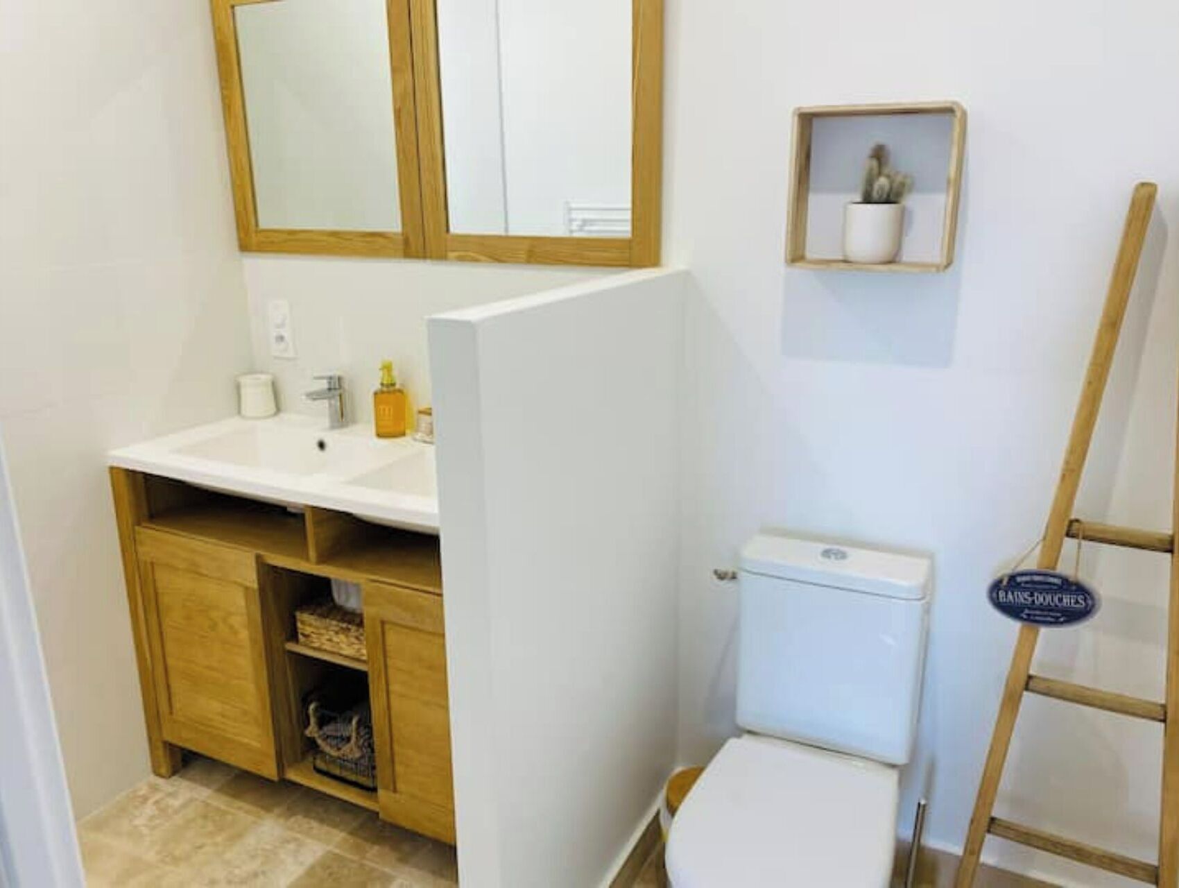 A bathroom with a white sink, wooden cabinet, toilet, and a small shelf with toiletries.