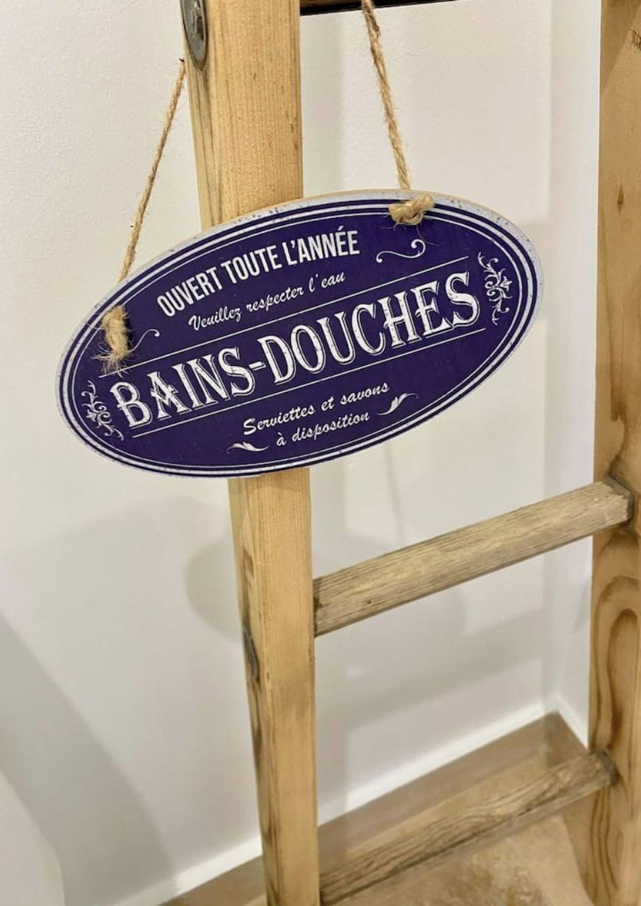 Une échelle en bois avec une pancarte indiquant : « OUVERT TOUT AU LONG DE L’ANNÉE. DOUCHES ET BAINS. Serviettes et savons à disposition. »