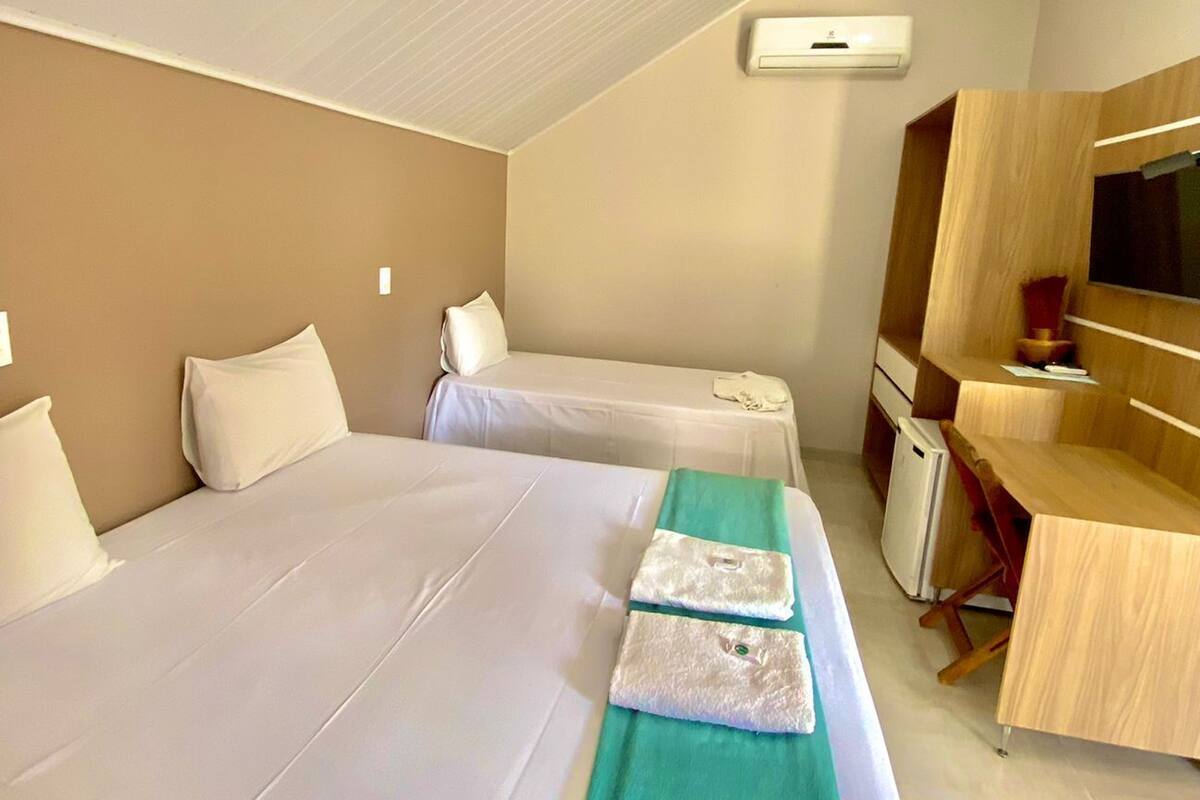 A hotel room with two beds, a desk, a mirror, and a television.