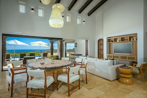 Enjoy ocean views from this spacious living area with a round dining table, comfortable sofa, and large flat-screen TV.