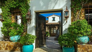 A traditional building with a tiled roof, a stone wall, and a wooden door. There are potted plants and lanterns on either side of the entrance.