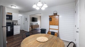 Eine kompakte Küche mit modernen Geräten, ein Essbereich mit einem Holztisch sowie eine eingebaute Holzküche mit Haken.