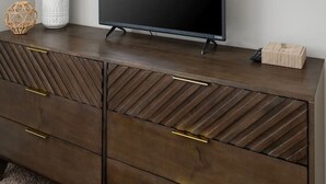 Ein modernes Wohnzimmer mit Flachbildfernseher, einer dekorativen Vase mit Pampasgras und einem geometrischen Wandbild.